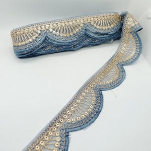 May include: A roll of blue decorative trim with a scalloped edge. The trim features a gold embroidered design with small sequins. The trim is likely used for embellishing clothing, accessories, or home decor projects.