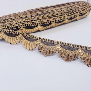 Könnte beinhalten: Goldene und braune Borte mit einem gewellten Rand. Die Borte ist aus Stoff und hat einen goldenen Metallic-Faden.