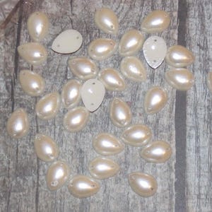 Può includere: Una collezione di decorazioni a forma di lacrima di colore bianco perlato. Le decorazioni sono in plastica e hanno una finitura liscia e lucida.