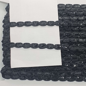 May include: Black sequined trim with a repeating oval pattern. The trim is shown on a white background.
