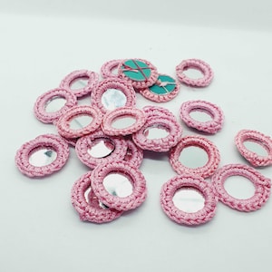 Könnte beinhalten: Ein Haufen rosa runder Häkelverzierungen mit kleinen Spiegeln in der Mitte.