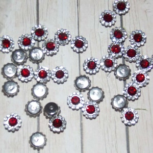 May include: A collection of red and silver rhinestones with a flower design. The rhinestones are scattered on a white wooden surface.