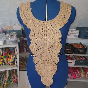 Puede incluir: Adorno de cuello de cuentas y bordado dorado con un delicado patrón floral. Este adorno es perfecto para agregar un toque de elegancia a cualquier prenda.