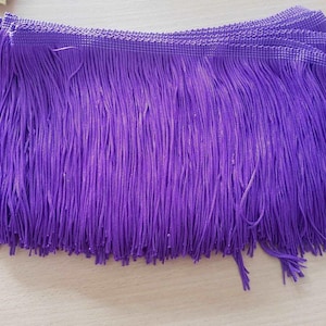 May include: Purple fringe trim with a woven texture. The fringe is approximately 2.5 cm long.