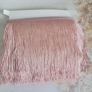 May include: A close-up of a pink fringe trim. The fringe is made of soft, thin strands of fabric.