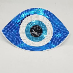 May include: Blue and white evil eye patch with sequins. The eye is surrounded by a white circle and a blue circle.