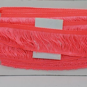 May include: Pink fringe trim with a woven base. The fringe is approximately 2.5 cm long.