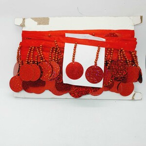May include: Red trim with a row of red sequins and beads. The trim is packaged on a white card with a sample of the trim attached.