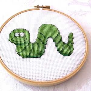 May include: A green embroidered worm with a smiling face in a wooden embroidery hoop.