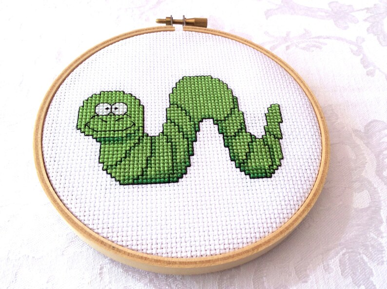 May include: A green embroidered worm with a smiling face in a wooden embroidery hoop.