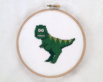 May include: A green and yellow cross-stitch embroidery of a cartoon dinosaur in a wooden embroidery hoop.