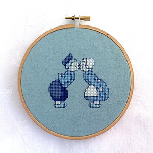 May include: A blue and white cross-stitch embroidery of a couple kissing, framed in a wooden hoop.