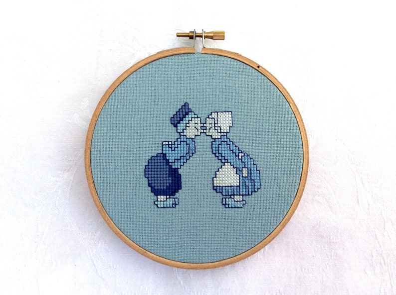 May include: A blue and white cross-stitch embroidery of a couple kissing, framed in a wooden hoop.