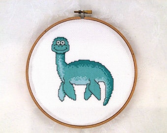 May include: A cross-stitch embroidery hoop with a smiling green dinosaur on a white background.