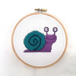 May include: A purple and teal snail cross-stitch embroidery in a wooden embroidery hoop.