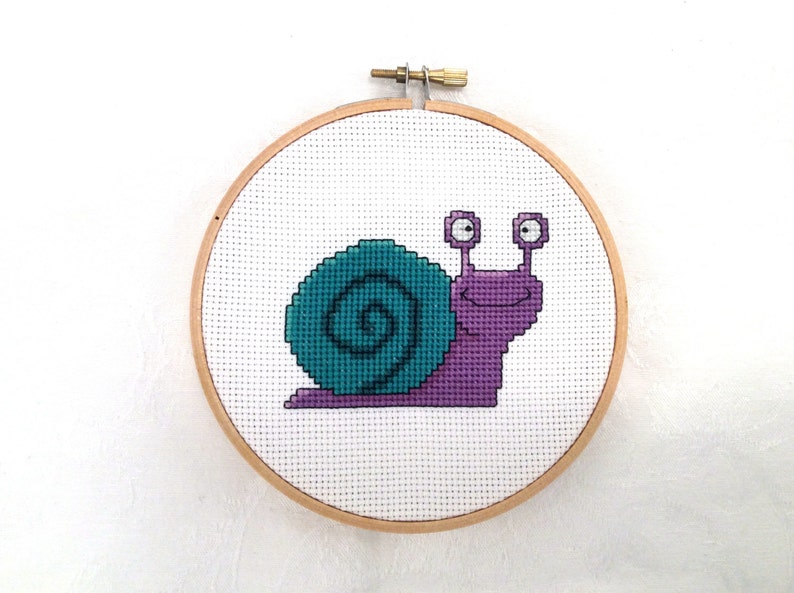 May include: A purple and teal snail cross-stitch embroidery in a wooden embroidery hoop.