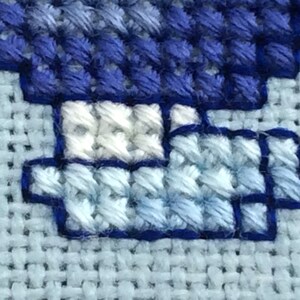 May include: Close-up of a blue and white cross-stitch design. The design features a blue and white pattern with a white border.