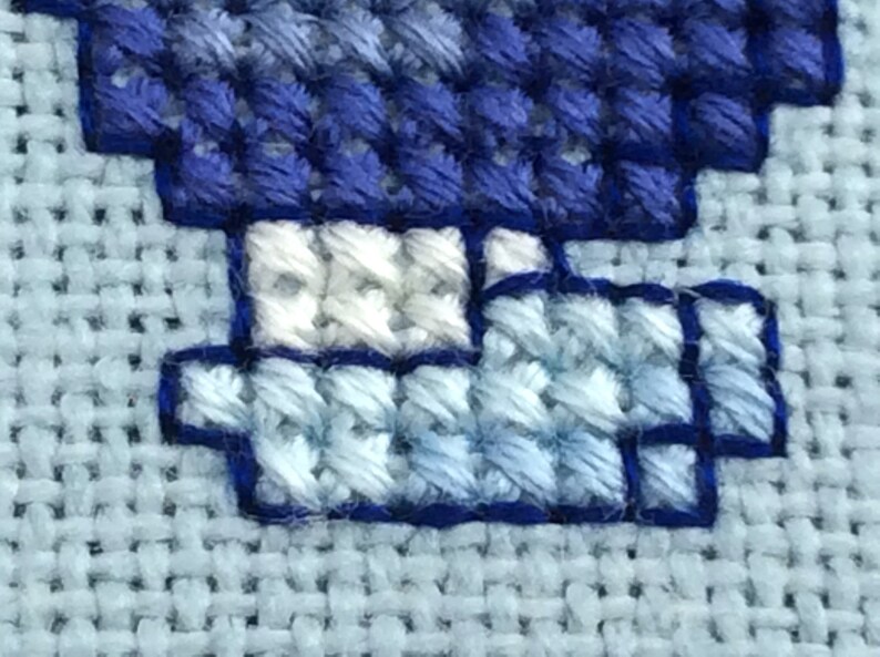 May include: Close-up of a blue and white cross-stitch design. The design features a blue and white pattern with a white border.
