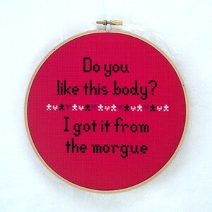 Op de afbeelding: Een rode borduurring met de tekst "Do you like this body? I got it from the morgue" in zwart garen.