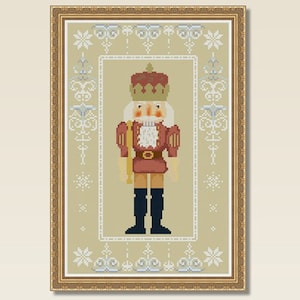 Puede incluir: Un patrón de punto de cruz de un cascanueces tradicional con un uniforme rojo y dorado, de pie sobre un fondo beige con un borde de copo de nieve blanco.