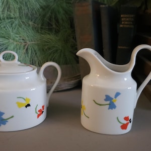 Peut inclure: Un ensemble sucrier et crémier en porcelaine blanche avec un motif floral. Les fleurs sont rouges, jaunes, bleues et vertes. L'ensemble est parfait pour ajouter une touche d'élégance à n'importe quelle table.