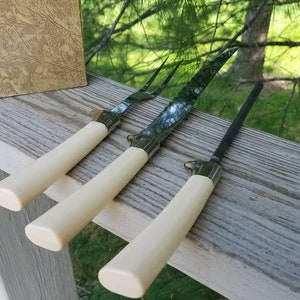 Puede incluir: Tres cuchillos de trinchar de acero inoxidable Sheffield con mangos de color marfil. Los cuchillos est&aacute;n dispuestos sobre una superficie de madera. La caja de los cuchillos es visible en el fondo. La caja es marr&oacute;n con letras doradas que dicen "Sheffield Stainless Carving Set" y "Forever Sharp".