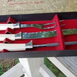 Puede incluir: Un juego de cuatro cuchillos y tenedores de plata en una caja forrada de terciopelo rojo. La caja es negra con las palabras "English Stainless Carving Set" y "Guaranteed Forever Sharp" impresas en la parte superior.