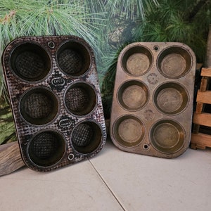 May include: Two vintage metal muffin tins with a dark brown patina. The tins have 6 individual muffin cups each. The tins are labeled "EKCO" and "VINEX".