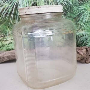 May include: A clear glass jar with a white lid. The jar has a square shape and a textured surface.