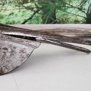 May include: A vintage metal potato masher with a long handle and a wide, flat head. The masher is made of silver-colored metal and has a worn, rustic appearance.