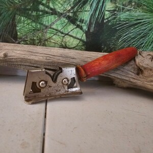 K&ouml;nnte beinhalten: Ein vintage Messersch&auml;rfer mit einem roten Holzgriff und zwei Metallr&auml;dern. Der Sch&auml;rfer ist aus Metall und tr&auml;gt die Aufschrift "Good Luck" und "U.S. Patent Office".