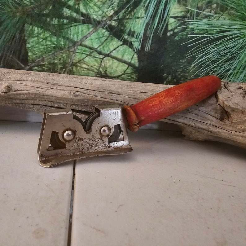 K&ouml;nnte beinhalten: Ein vintage Messersch&auml;rfer mit einem roten Holzgriff und zwei Metallr&auml;dern. Der Sch&auml;rfer ist aus Metall und tr&auml;gt die Aufschrift "Good Luck" und "U.S. Patent Office".