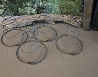 May include: Four antique metal bed springs with a spiral design. The springs are a faded blue color and have a circular base. The background includes a piece of driftwood, books, and a wooden crate.
