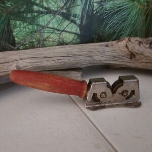 K&ouml;nnte beinhalten: Ein vintage Messersch&auml;rfer mit einem roten Holzgriff und zwei Metallr&auml;dern. Der Sch&auml;rfer ist aus Metall und hat eine silberne Oberfl&auml;che.