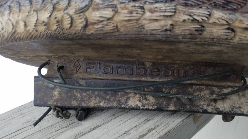 May include: A close-up of a brown duck decoy with a metal base. The base is labelled "Flambeau".