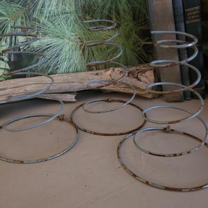 May include: Close-up of several antique metal bed springs with a spiral design. The springs have a distressed, rusty appearance, with circular bases. The background includes a piece of driftwood, books, and wooden planks.