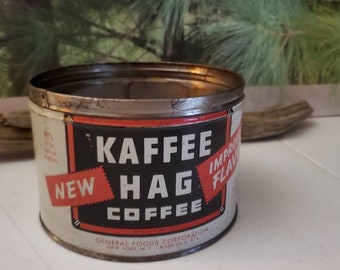Op de afbeelding: Vintage Kaffe Hag Koffie blik. Het cilindrische blik heeft een witte achtergrond met een zwart en rood etiket. Op het etiket staat "KAFFEE HAG COFFEE" en "NEW IMPROVED FLAVOR". Het blik is gemaakt door General Foods Corporation.
