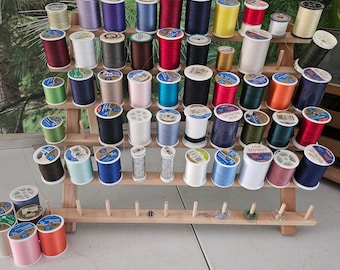 May include: A wooden thread rack with multiple spools of thread in various colors, including red, blue, green, and yellow. The rack has two shelves and is made of natural wood.