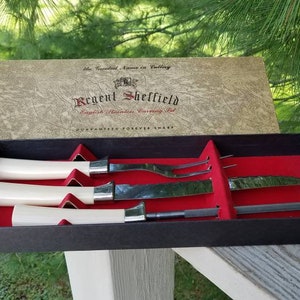 Puede incluir: Un juego de cuatro cuchillos de plata con mangos de marfil en una caja negra con forro de terciopelo rojo. La tapa de la caja est&aacute; abierta y presenta el texto "Regent Sheffield English Stainless Cutlery Set Guaranteed Forever Sharp".