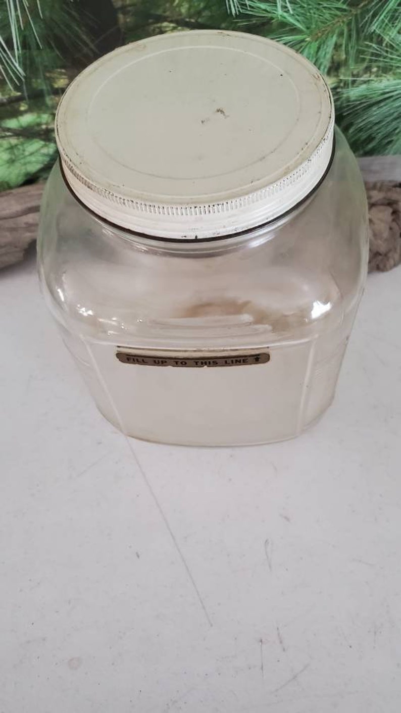 May include: A clear glass jar with a white lid and a brown label that reads "Fill up to this line".