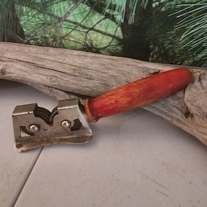K&ouml;nnte beinhalten: Ein vintage Messersch&auml;rfer mit einem roten Holzgriff und drei Schleifscheiben aus Metall. Der Sch&auml;rfer ist aus Metall und hat eine leicht gebogene Form.