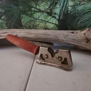 K&ouml;nnte beinhalten: Ein vintage Messersch&auml;rfer mit einem roten Holzgriff und drei Schleifscheiben aus Metall. Der Sch&auml;rfer ist aus Metall und hat eine silberne Oberfl&auml;che.