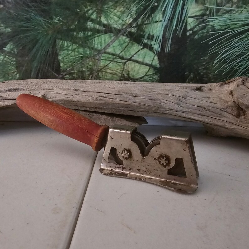 K&ouml;nnte beinhalten: Ein vintage Messersch&auml;rfer mit einem roten Holzgriff und drei Schleifscheiben aus Metall. Der Sch&auml;rfer ist aus Metall und hat eine silberne Oberfl&auml;che.