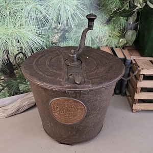 May include: An antique, cylindrical, metal ice cream maker with a hand crank and a copper-colored label that reads "UNIVERSAL ICE CREAM MAKER". The ice cream maker is a rusty brown color and has two handles. The image is of a vintage kitchen appliance.
