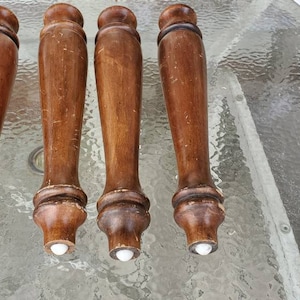 May include: Four wooden table legs with white plastic tips. The legs are brown and have a smooth finish.