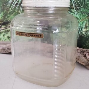 May include: A clear glass jar with a white lid and a label that reads "Fill up to this line".