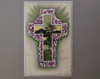 May include: A vintage Easter greeting card with a cross made of purple flowers. The cross is surrounded by a green background with a landscape scene in the center. The text "Best Wishes for Easter" is printed below the cross.