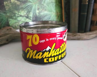 Op de afbeelding: Een vintage metalen koffieblik in rood, geel en zwart met de tekst "70 kopjes in elk pond Manhattan Coffee".