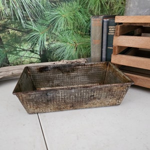 May include: A vintage, rectangular metal baking pan with a textured surface. The pan is slightly rusted and has a worn, antique look.