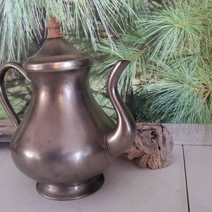 May include: A silver teapot with a wooden knob on the lid. The teapot has a rounded body and a spout on the side.